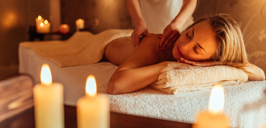 Eine junge Frau genießt bei Kerzenschein eine Rückenmassage in einem Wellness-Bereich