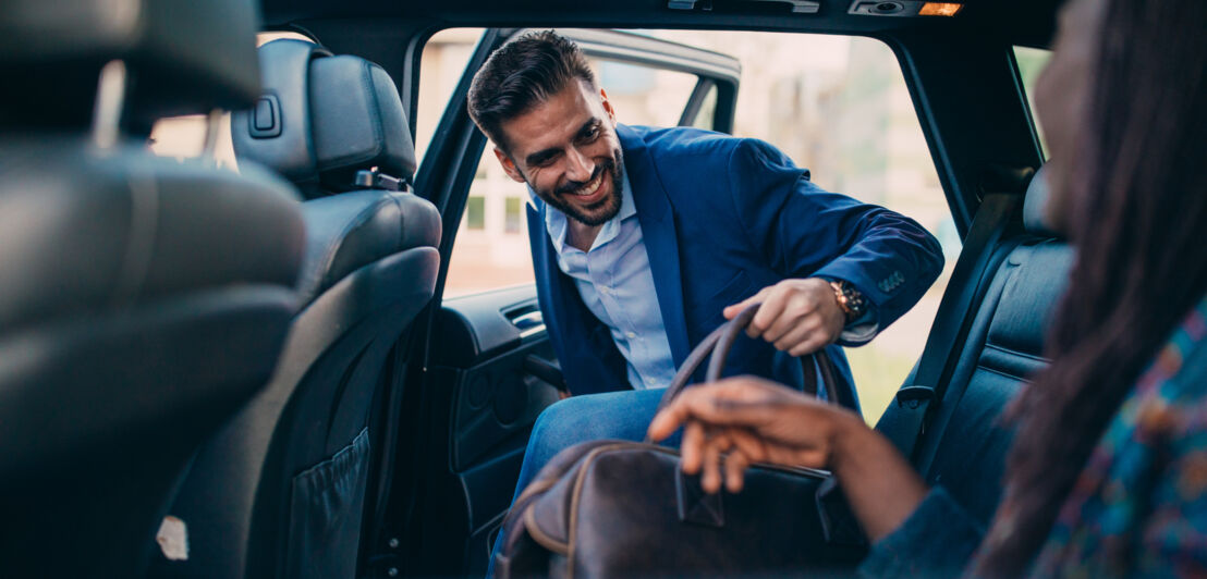 Ein elegant gekleideter Mann steigt mit einer Reisetasche auf den Rücksitz eines Autos ein