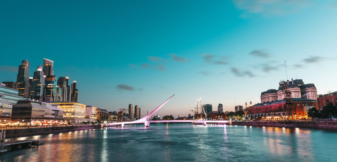 Hafengebiet in Buenos Aires mit beleuchteter Brücke und Hochhäusern im Hintergrund bei Abenddämmerung