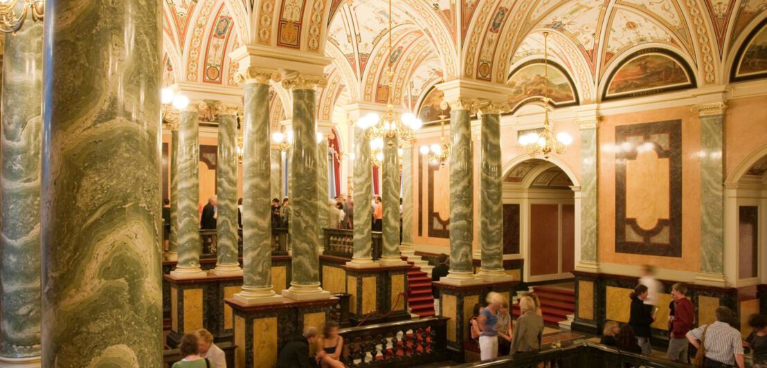 Beleuchtetes Foyer der Semperoper mit Marmorsäulen und Publikum