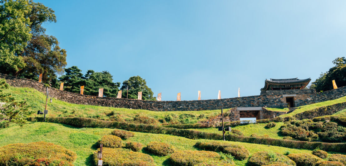 Eine begrünte Festungsanlage mit Steinmauer und Stadttor im koranischen Baustil