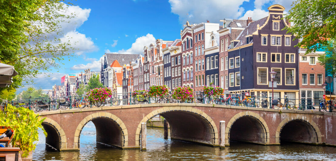 Historische Giebelhäuser an einer mit Blumen dekorierten Brücke über einer Gracht.