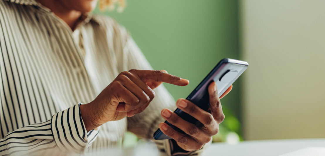 Nahaufnahme von zwei Händen einer Frau, die an einem Schreibtisch ihr Smartphone bedient