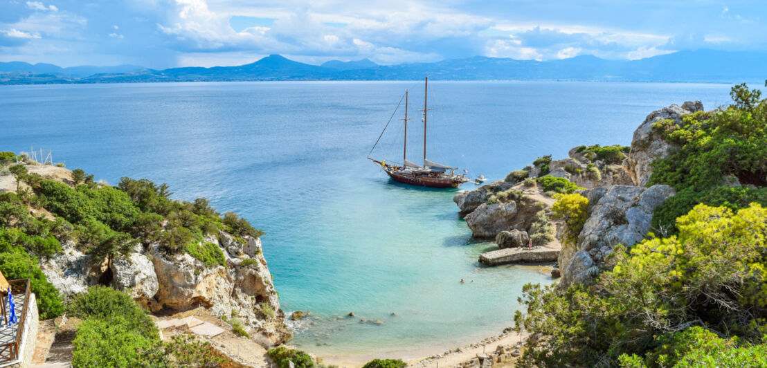 Ein Segelboot ankert vor einer kleinen Felsbucht mit Sandstrand