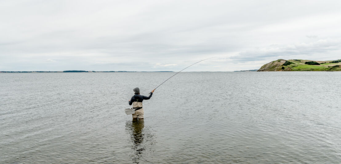 Eine Person steht bis zur Hüfte im Wasser und angelt