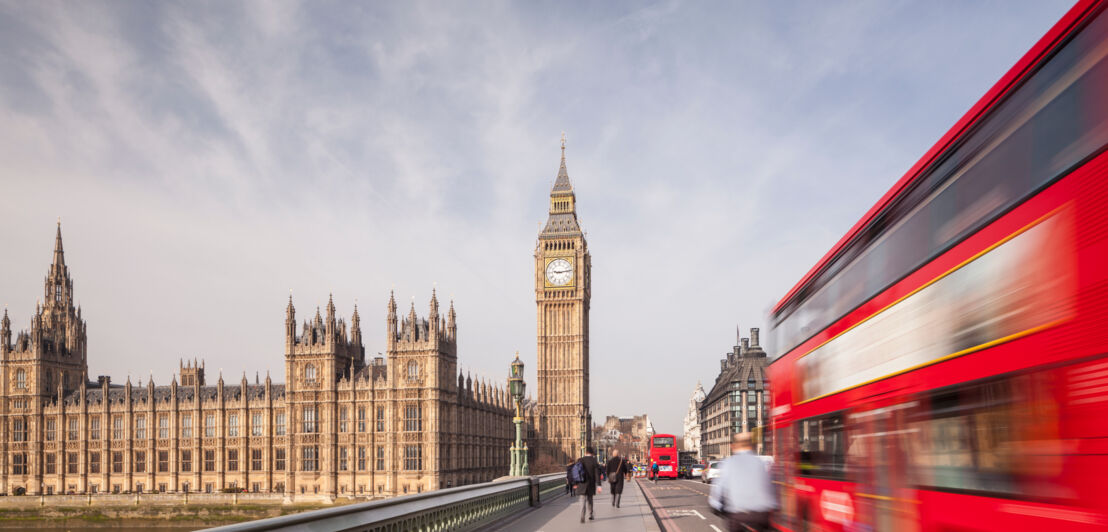 Big Ben und Houses of Parliament am Ende einer Brücke, auf der rote Doppeldeckerbusse fahren