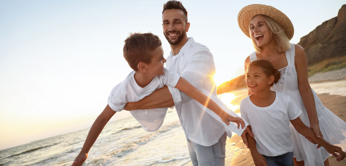 Eine hell gekleidete, glückliche Familie mit zwei Kindern am Strand bei Sonnenuntergang.