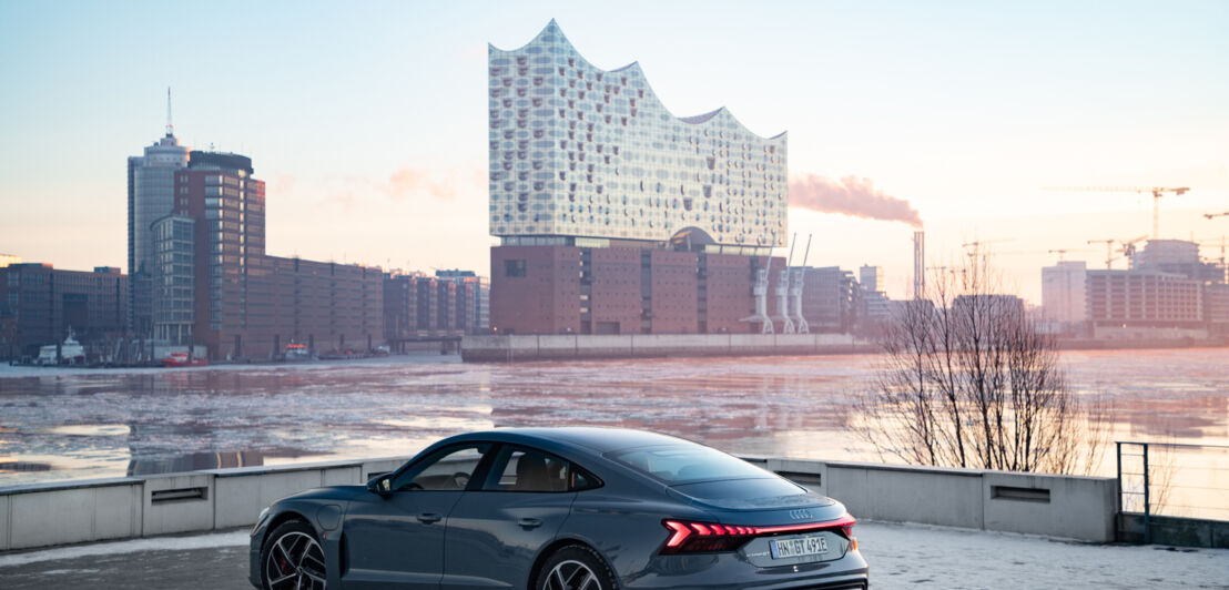 Ein AUDI e-tron GT an der Elbe in Hamburg, im Hintergrund die Elbphilharmonie