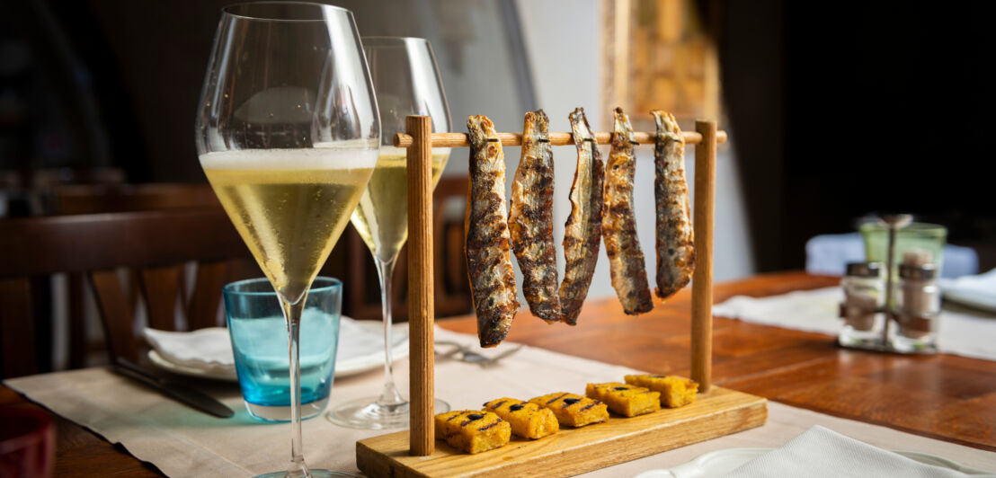 Zwei Gläser mit perlendem Schaumwein auf einem gedeckten Tisch mit Snacks