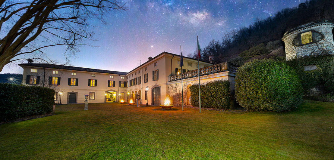 Beleuchtetes, herrschaftliches Gebäude eines Weingutes mit Gartenanlage am Abend