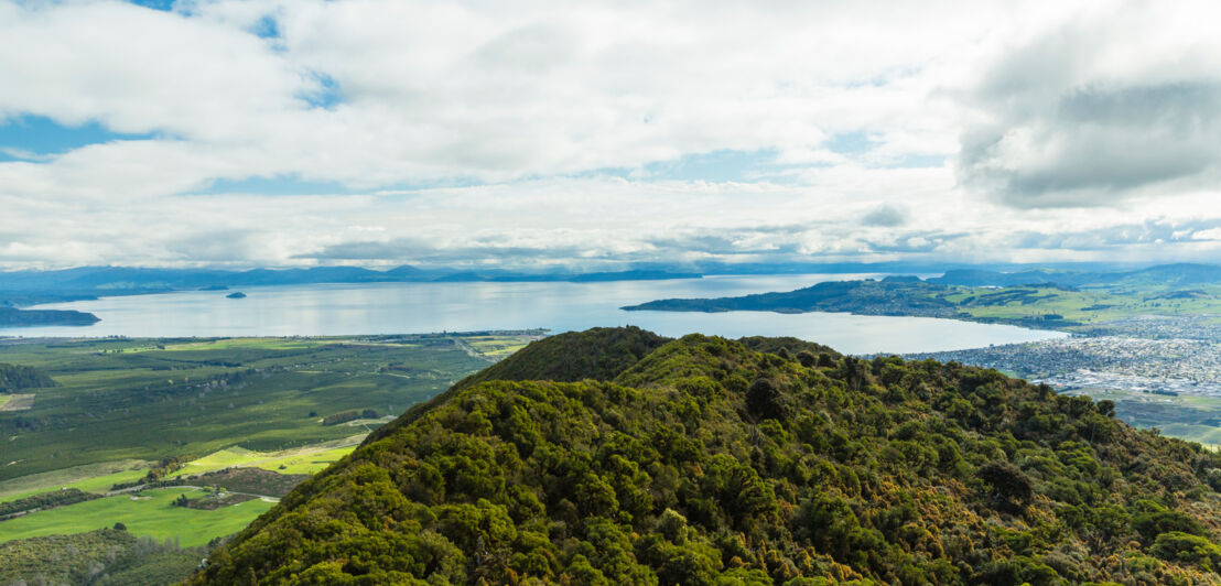 Blick über einen bewaldeten Bergkamm hin zu einem großen See