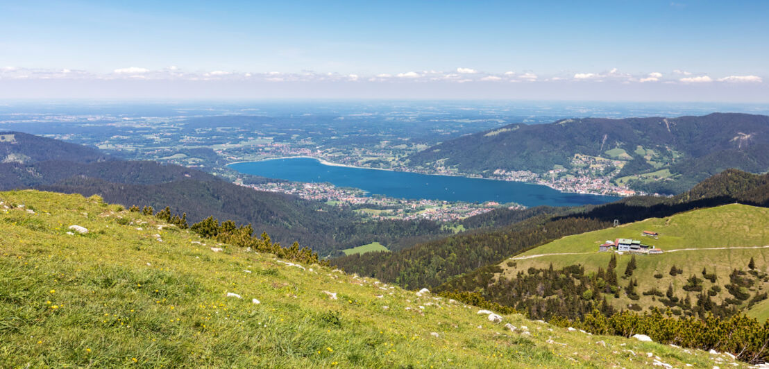 Panoramablick auf den Tegernsee von einer grasbewachsenen Bergkuppe aus.