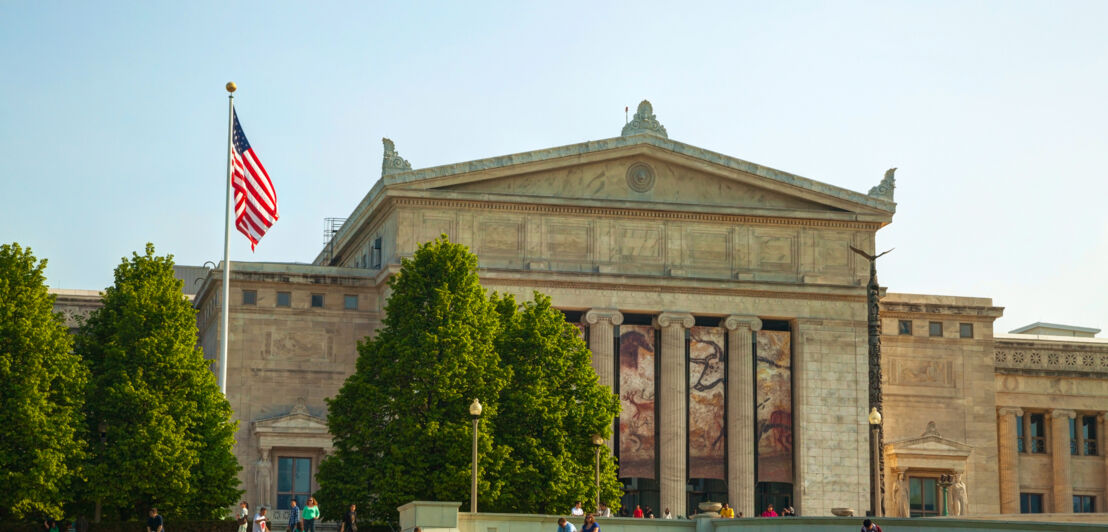 Imposantes Museumsgebäude im neoklassizistischen Baustil, davor eine wehende US-amerikanische Flagge und Personen auf einer Wiese.