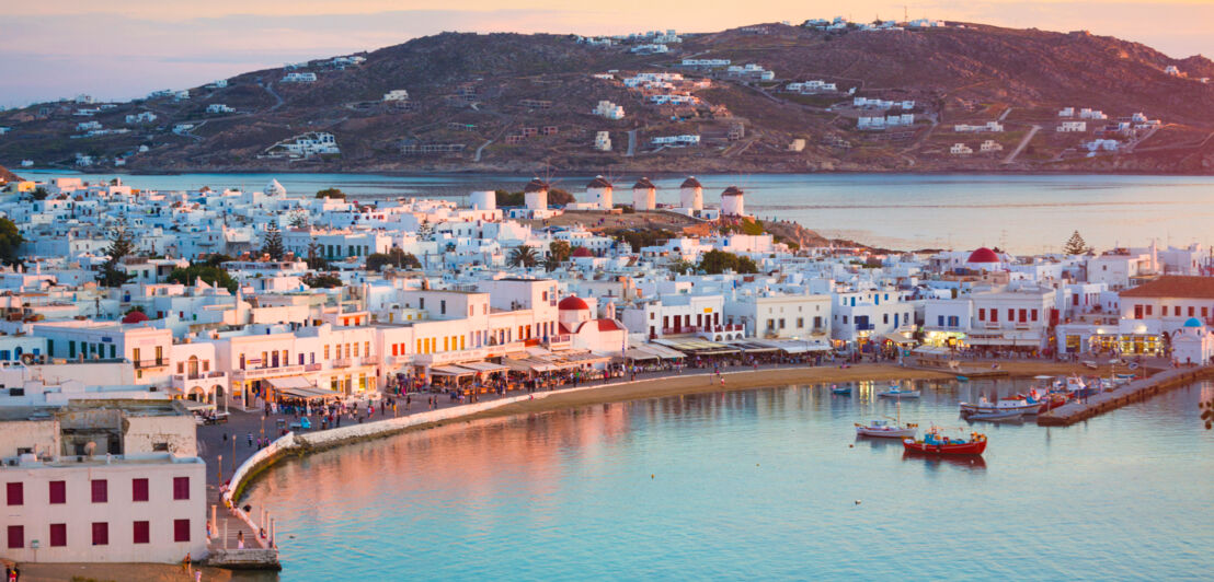 Mykonos-Stadt mit weißen Häusern und belebter Uferpromenade bei Abenddämmerung. 