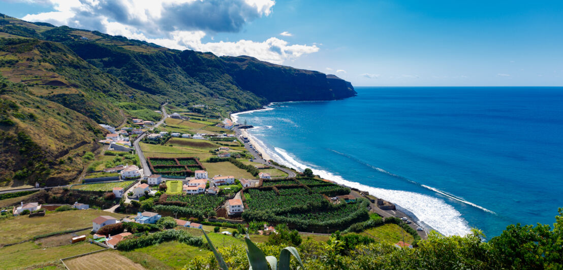 Malerische Bucht mit Sandstrand und vereinzelten Häusern und landwirtschaftlichen Parzellen.