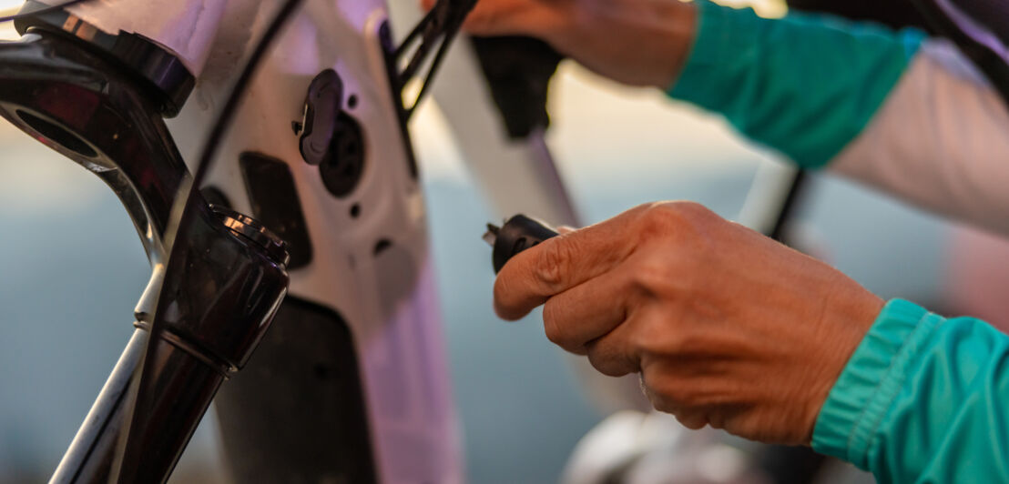 Nahaufnahme einer Hand mit Ladekabel an einem E-Bike.