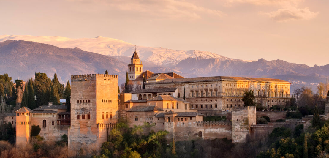 Palastkomplex der Alhambra auf einem Plateau vor Bergpanorama am Abend.