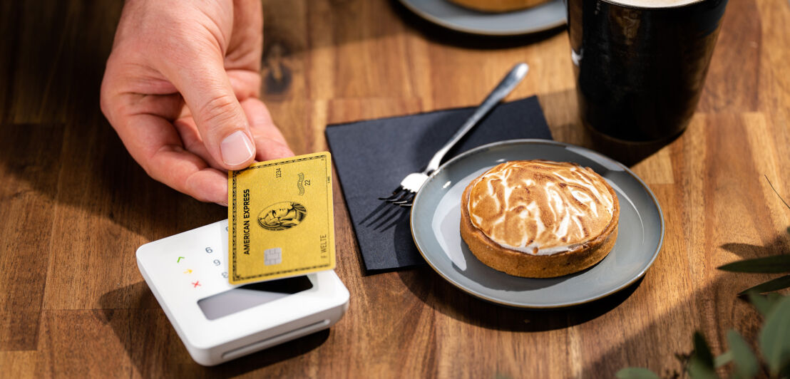 Eine Person bezahlt kontaktlos mit einer American Express Gold Card in einem Café.