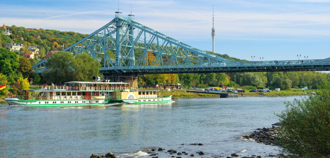 Blick vom Ufer auf das Blaue Wunder, unter dem ein Flussdampfer hindurchfährt.