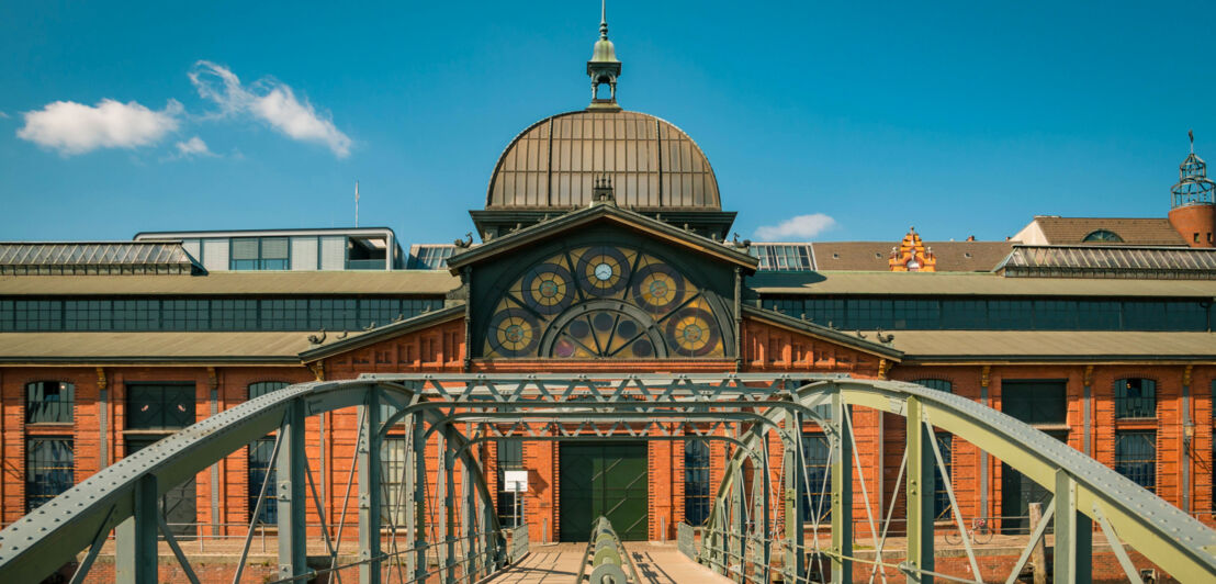 Fassade der Fischauktionshalle in Hamburg, zu dessen Backsteingebäude mit Kuppel und Fassadenverzierung eine Brücke führt.