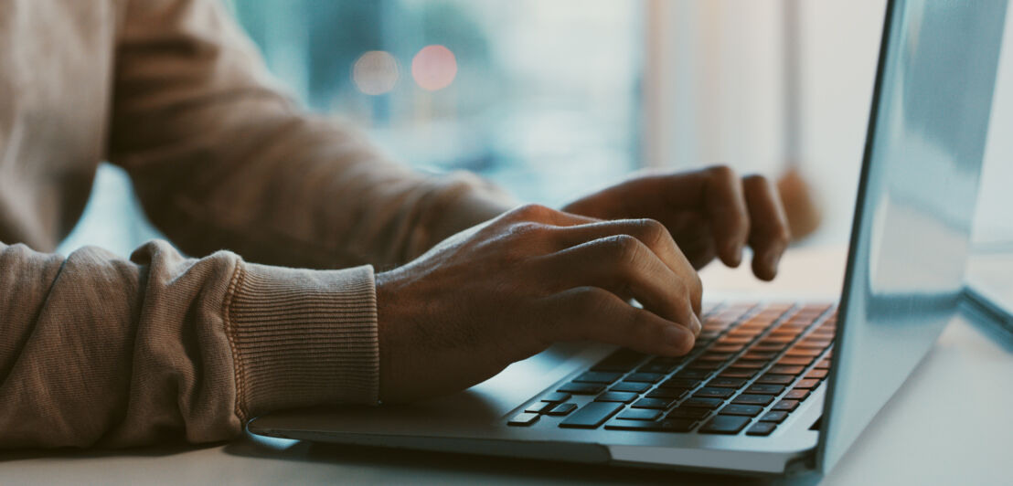 Nahaufnahme einer Person, die etwas auf der Tastatur eines aufgeklappten Laptops tippt.