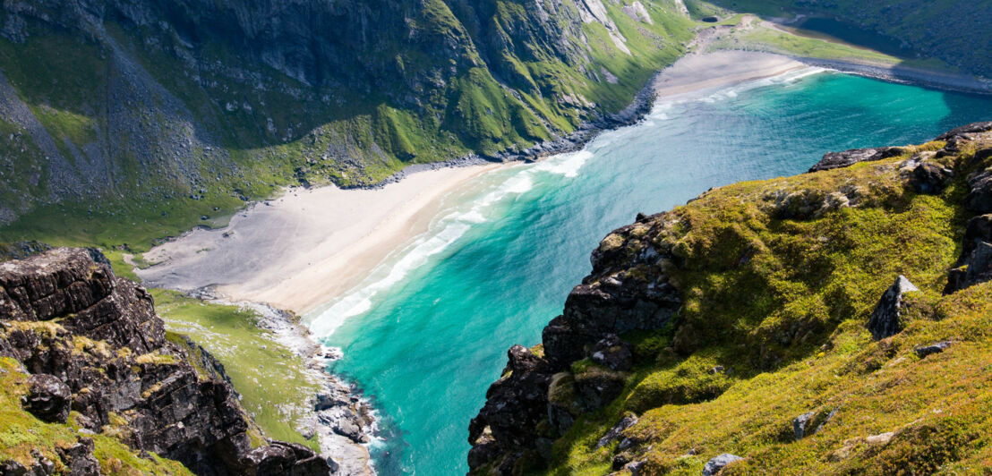 Luftaufnahme des Kvalvika Beach auf den norwegischen Lofoten, der von grün bewachsenen Felsen umgeben ist.