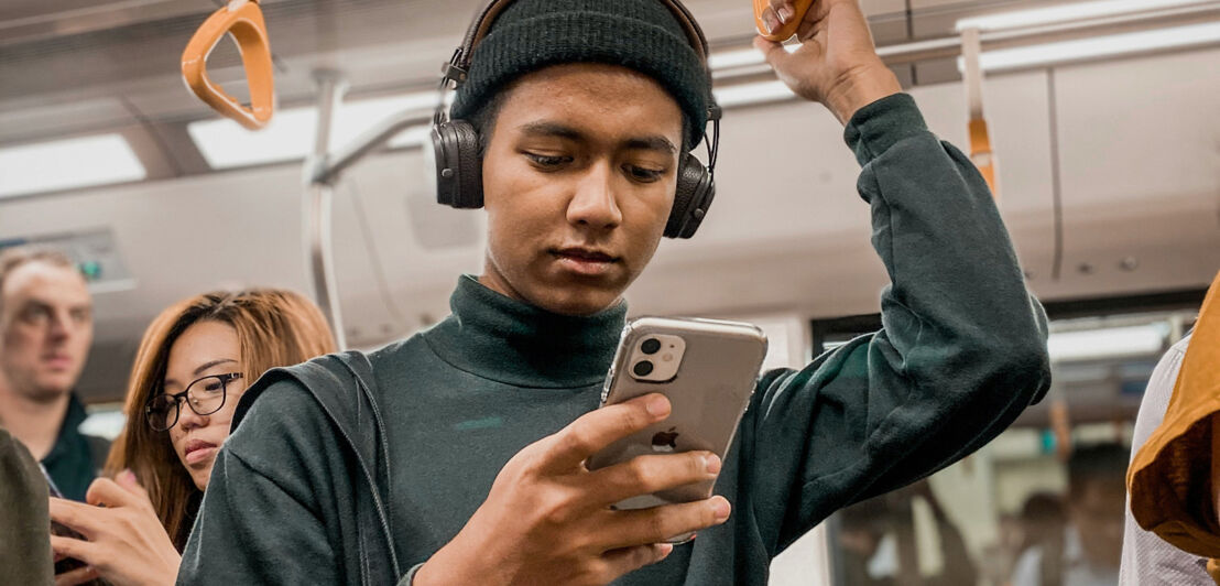 Junger Mann in der U-Bahn liest auf seinem Smartphone