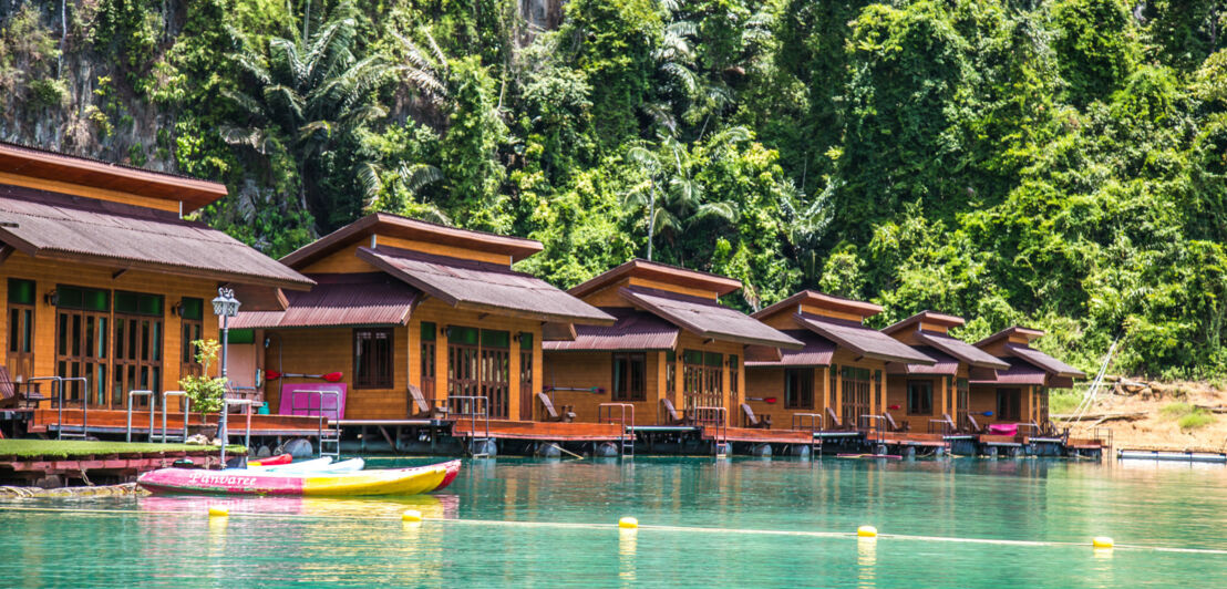 Mehrere hölzerne Floating Bungalows nebeneinander auf dem türkisfarbenen Chiao-Lan-See