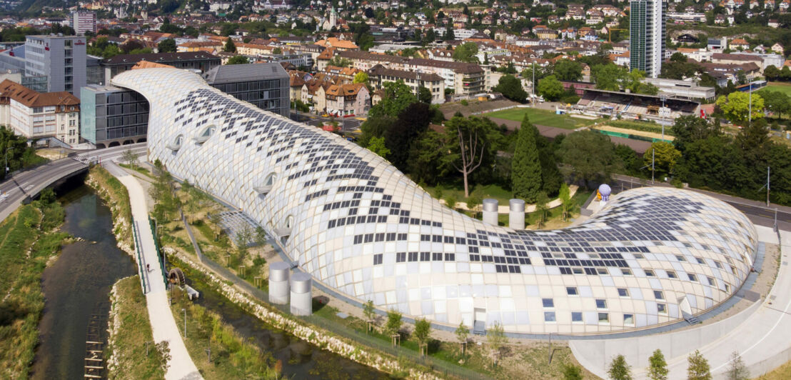 Panorama einer Kleinstadt mit futuristischem Gebäudekomplex in Schlangenform.