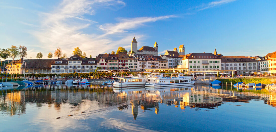 Ortschaft mit Burg an einem See mit Booten bei Sonnenschein.