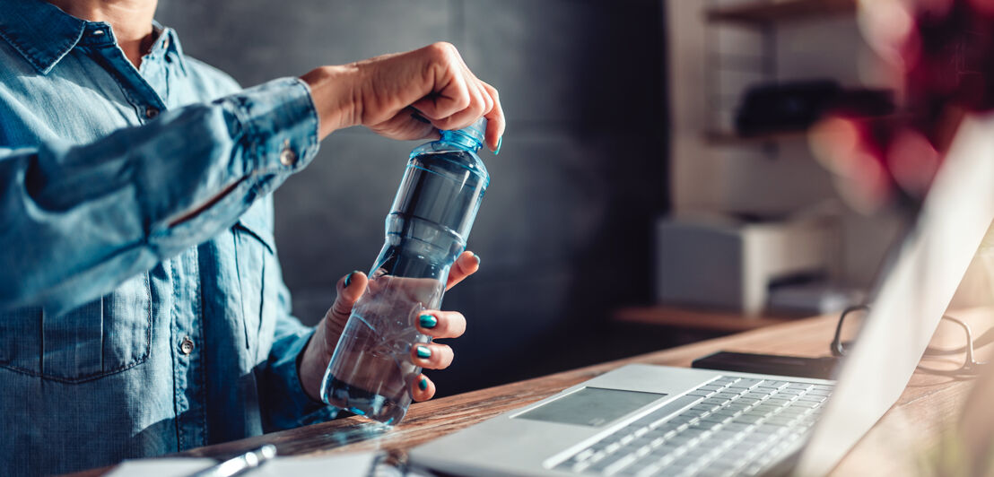 Frau im Home-Office öffnet eine Wasserflasche