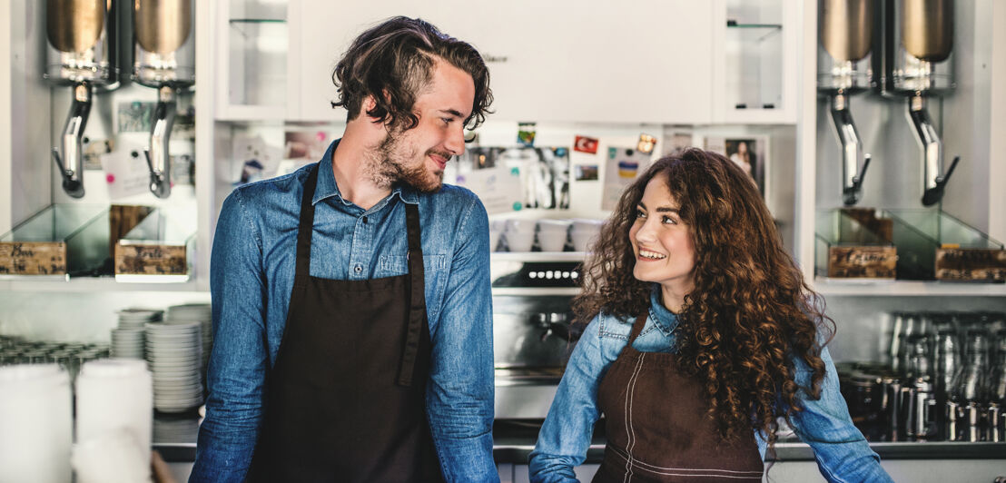 Zwei junge Barista im eigenen Café lächeln sich an