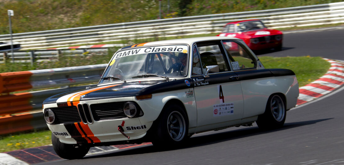 Ein fahrender BMW 2002 ti Rennwagen in der Kurve einer Rennstrecke, dahinter ein weiterer Rennwagen.