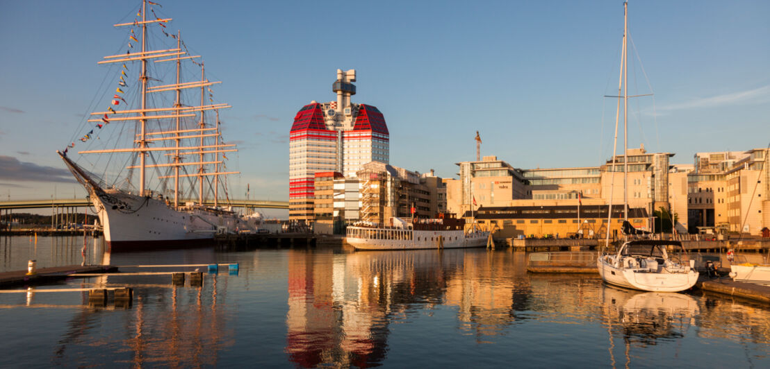 Anlagestelle im Hafen von Göteborg bei Sonnenuntergang mit verschiedenen Schiffen und dem Skanskaskrapan-Hochhaus im Hintergrund.