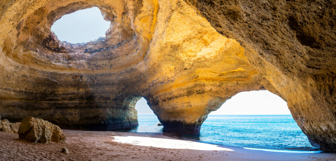 Innenraum der Meereshöhle Algar de Benagil an der Algarve, in dessen Decke ein Loch im Gestein ist, durch das die Sonne scheint.