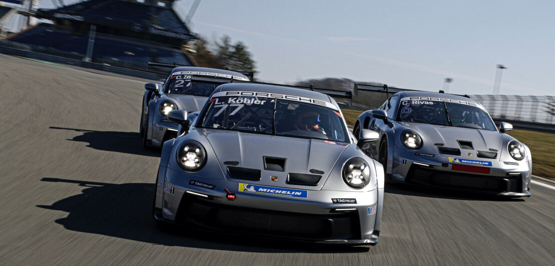 Drei silberne Porsche Rennwagen auf einer Rennstrecke.