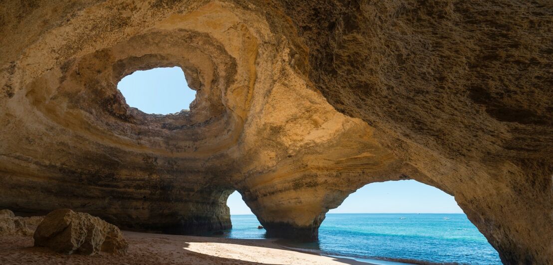 Der Innenraum der Meereshöhle Algar de Benagil mit drei großen Löchern, durch die das Meer und der Himmel zu sehen sind.