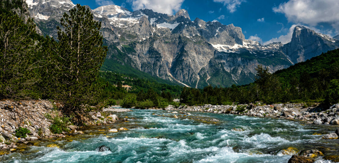 Fluss im Nationalpark Theth in Albanien mit schneebedeckten Gipfel im Hintergrund.