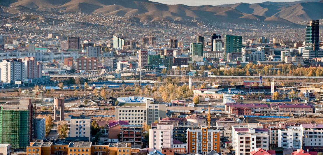 Fernaufnahme der Häuser von Ulaanbataar, der Hauptstadt der Mongolei, mit Gebirge im Hintergrund.