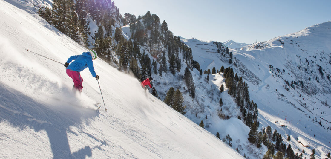 Zwei Skifahrende bei der Abfahrt auf einer steilen Piste.