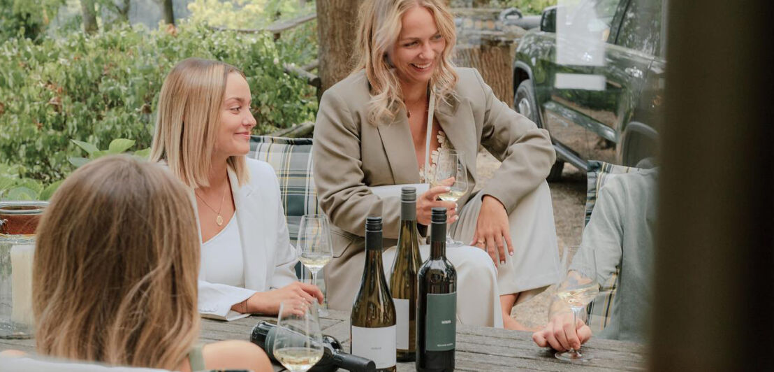 Foto von zwei jungen Frauen, die sich mit einem Glas Wein in der Hand unterhalten.