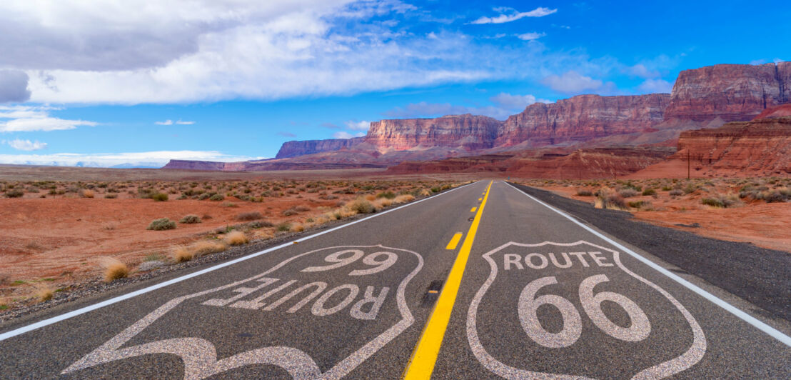 US-amerikanische Autobahn mit Route 66 Markierung auf der Fahrbahn in Felswüste mit rotem Sandboden.