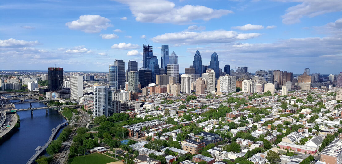 Skyline von Philadelphia mit niedrigen Häusern in begrüntem Wohnviertel vor Hochhäusern im Hintergrund.