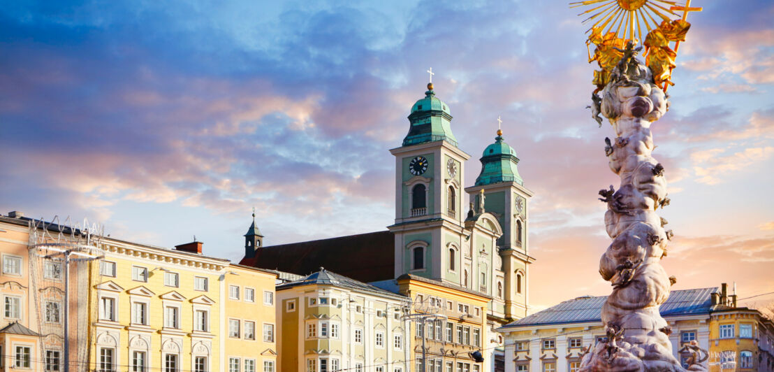 Ein Platz in Linz mit alten Häusern, im Vordergrund die barocke Dreifaltigkeitssäule.