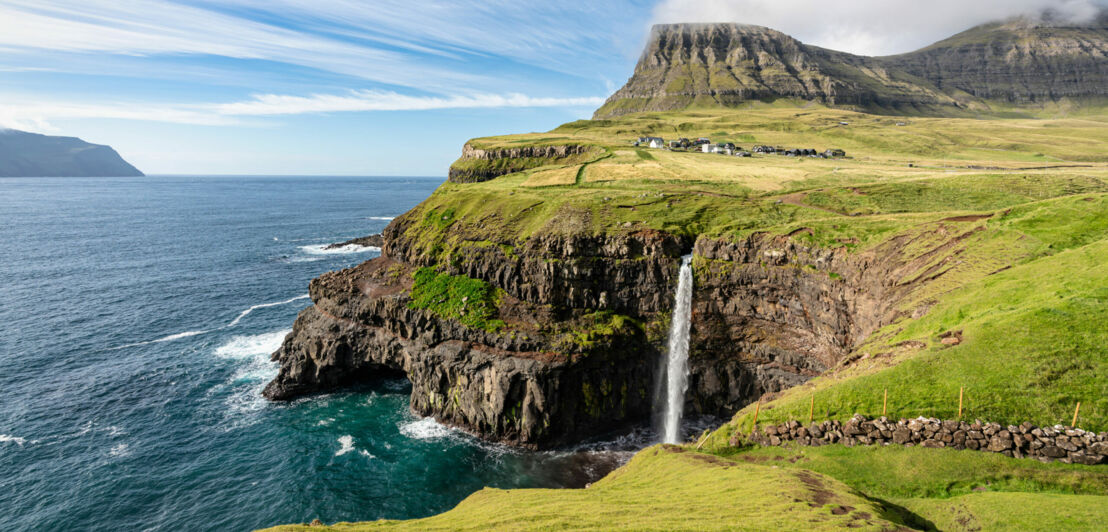 Ein Wasserfall auf einer mit Gras bewachsenen Felseninsel stürzt eine Klippe hinab ins Meer.