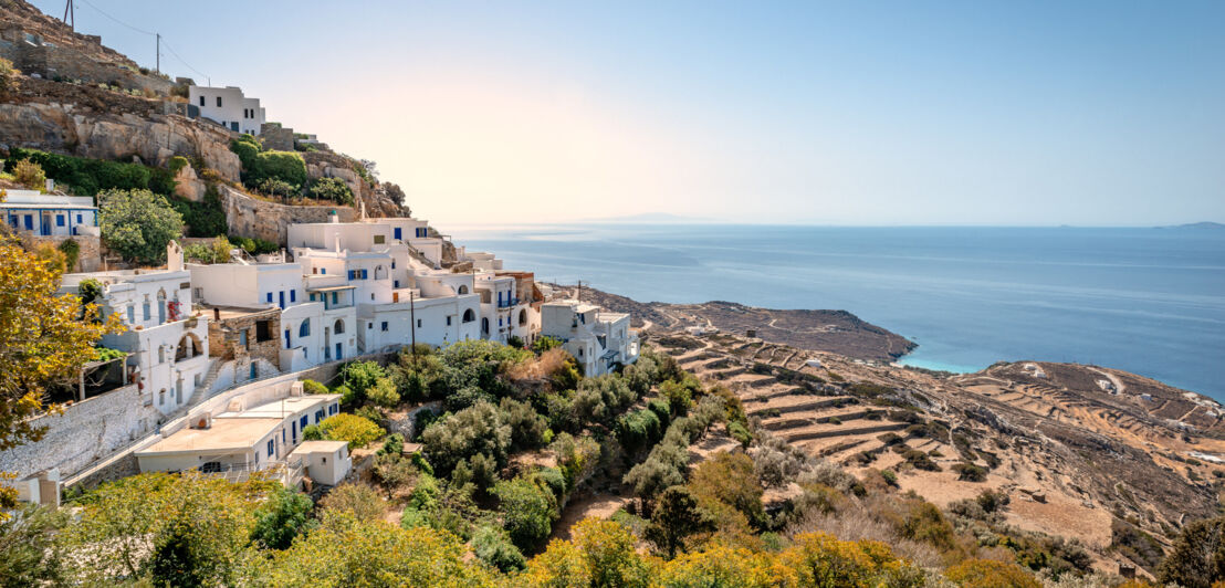 Weiße Häuser im griechischen Stil an einem Hang mit Blick aufs Meer.