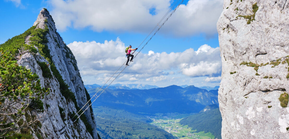 Eine Person auf einer Leiter zwischen zwei Felsen über einem grünen Tal.