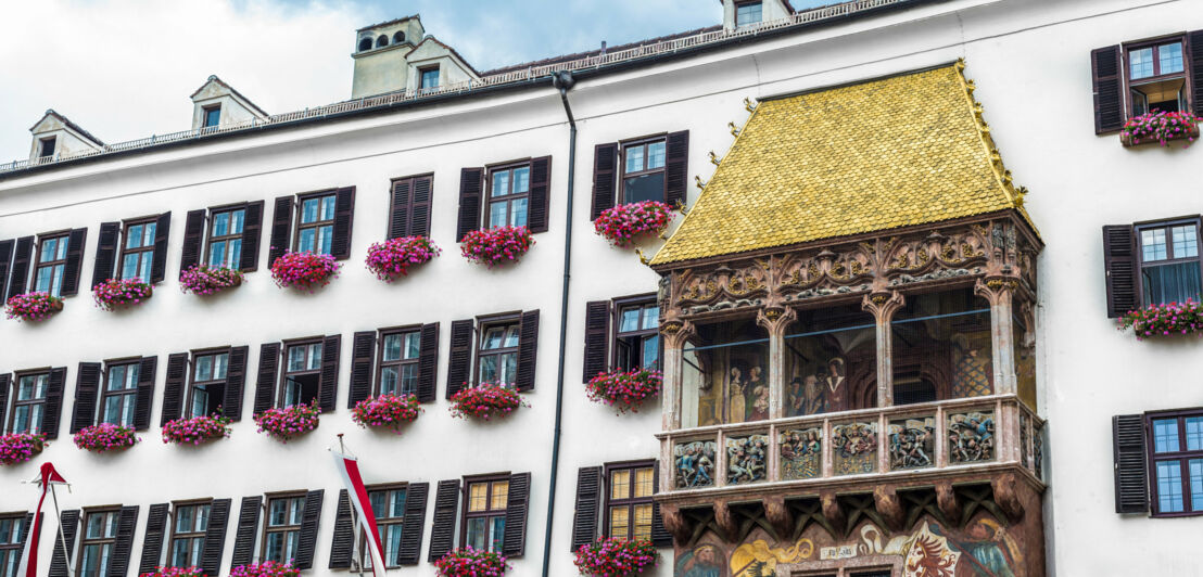 Hausfassade mit Balkon mit prunkvollen Verzierungen und goldenem Dach.