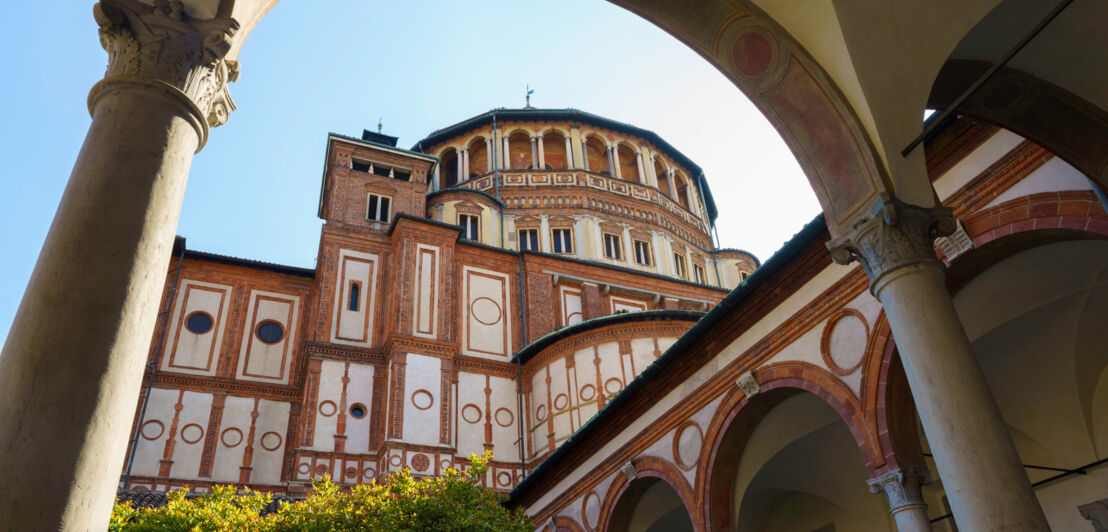 Blick auf ein rundes Klostergebäude durch einen Bogen im Kreuzgang.