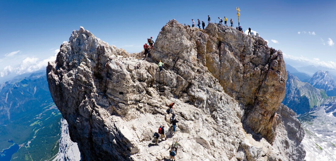 Wandernde auf dem Gipfel der Zugspitze bei blauem Himmel.